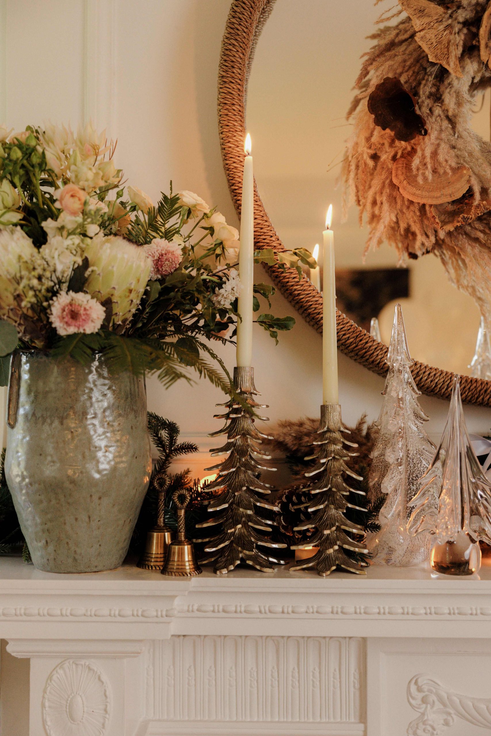 A mantel decorated for the holidays with taper candles, Simon Pierce glass Christmas trees, and fresh florals