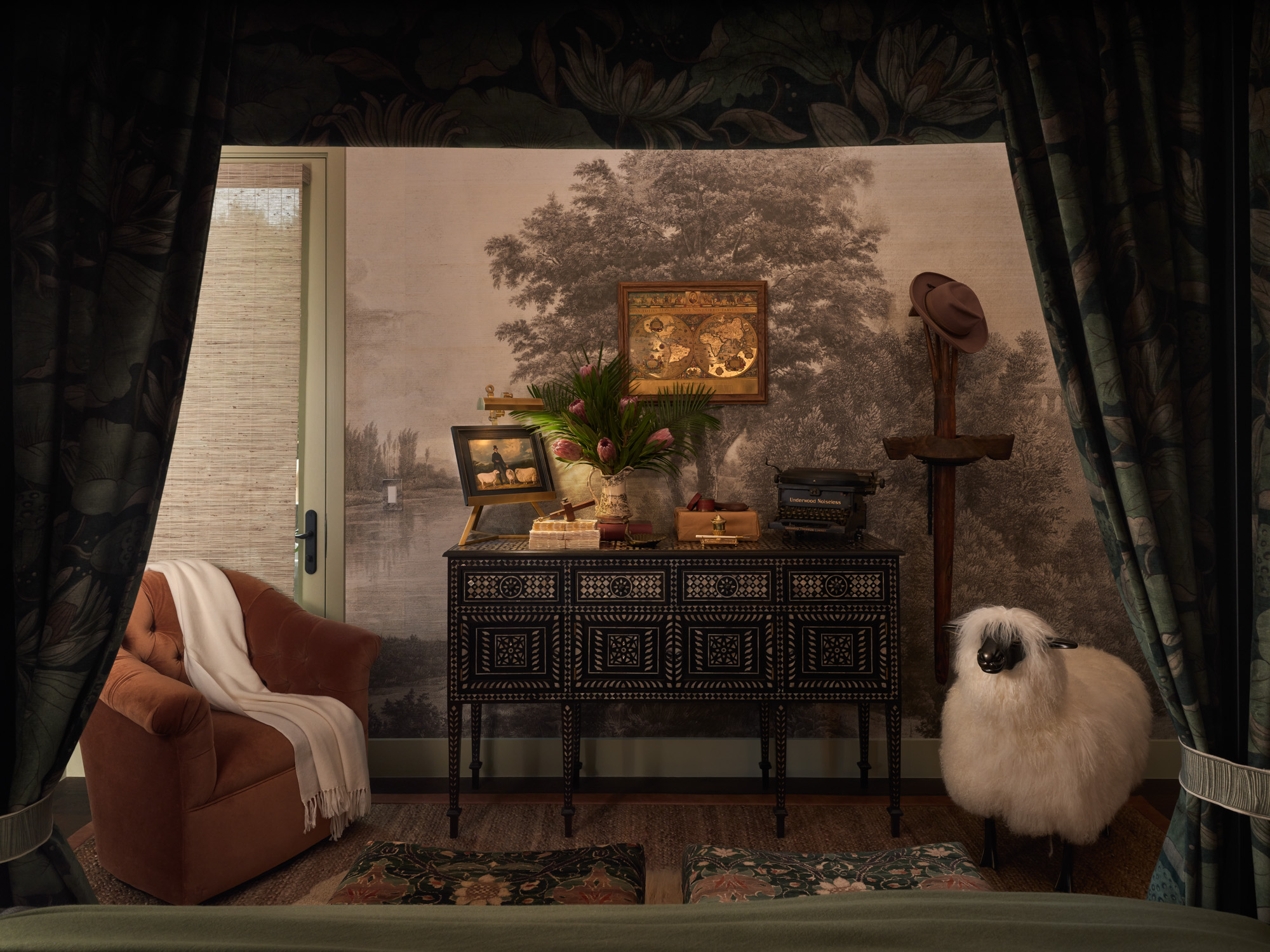 A cozy primary bedroom with a four-poster canopy bed, layered rugs, patterned ottomans, and soft, layered bedding