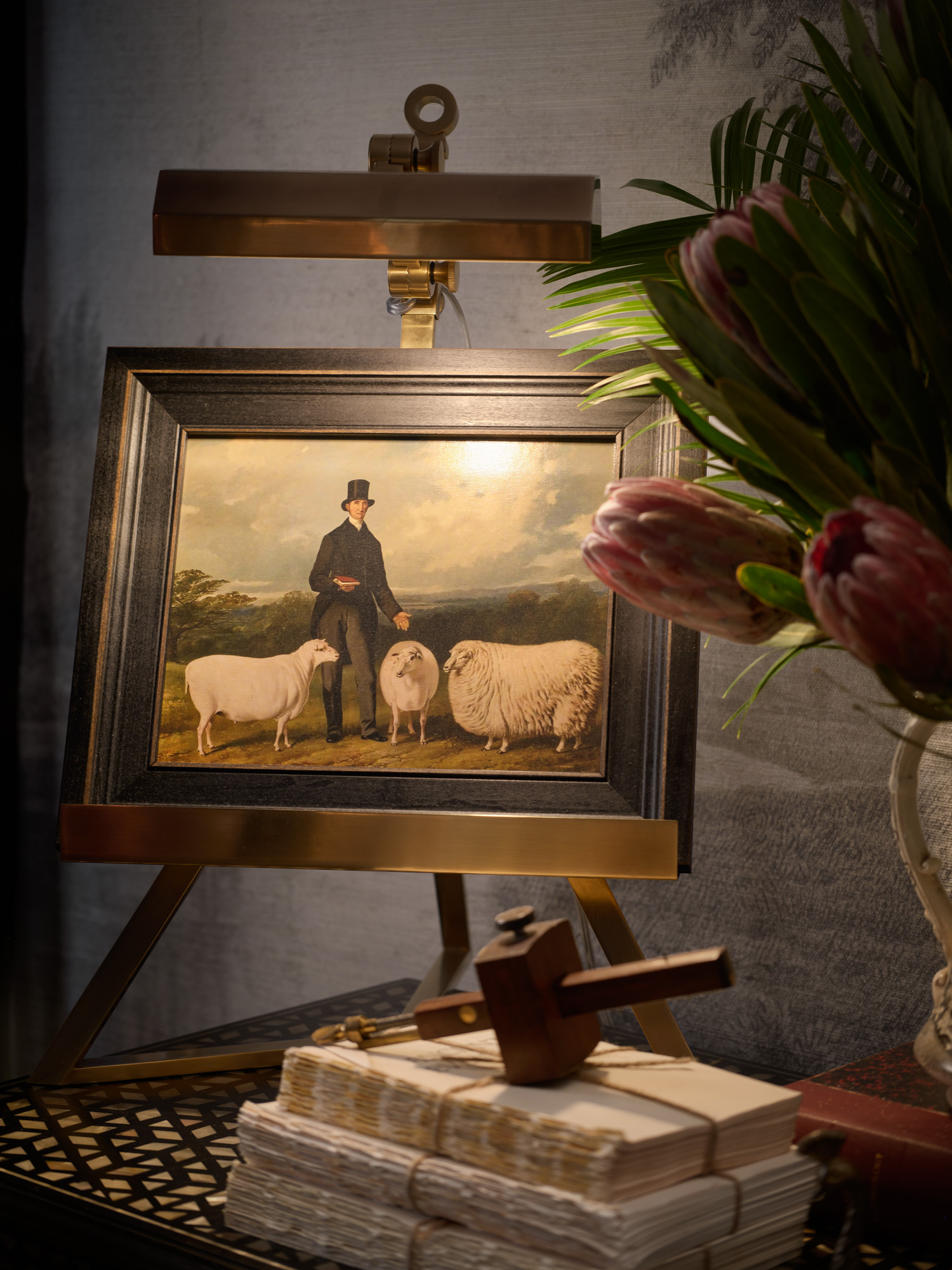 A small framed painting sits on a picture light easal in a primary bedroom