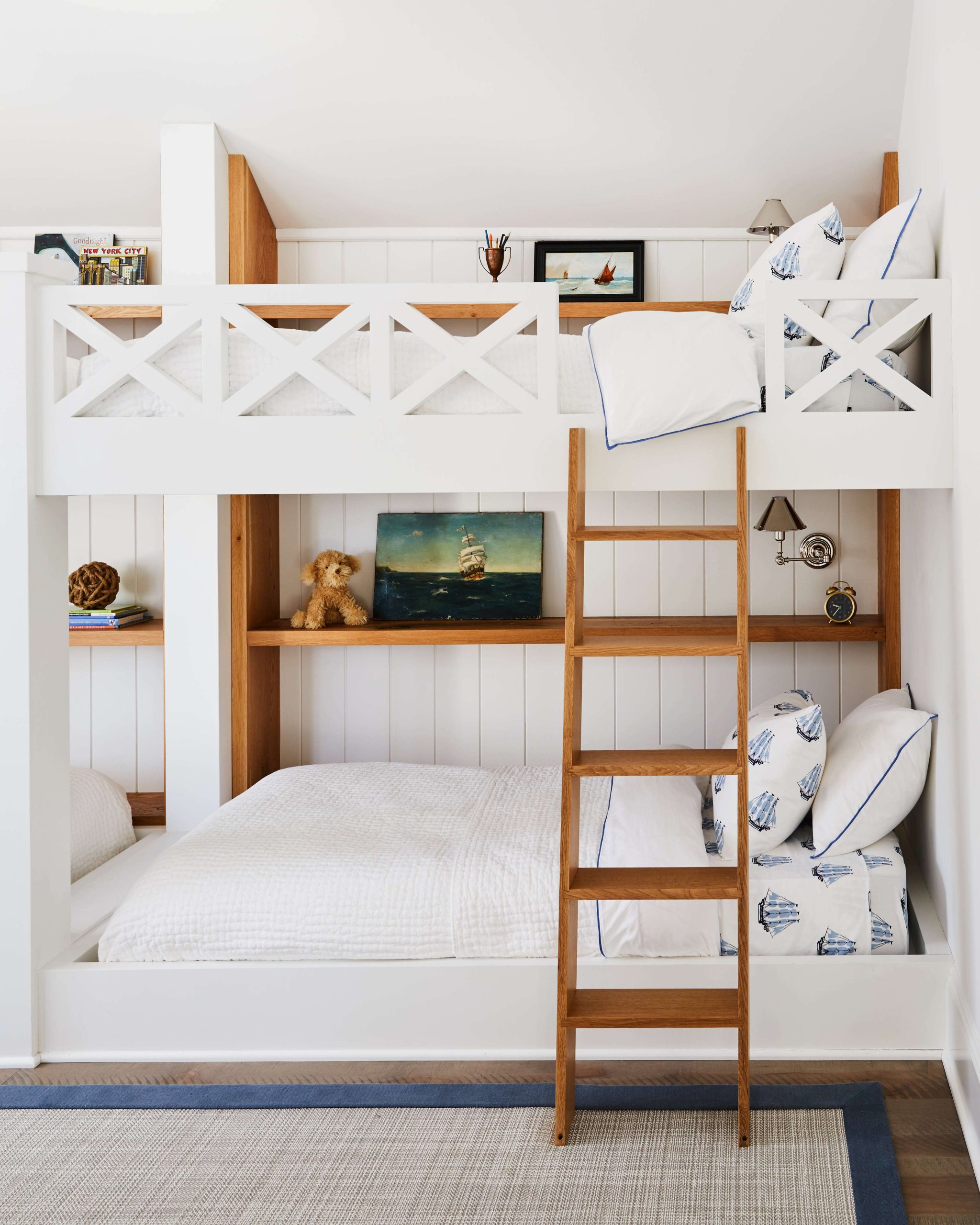 a coastal style kids room with a white bunk bed, a brown wood ladder, and coastal-inspired artwork