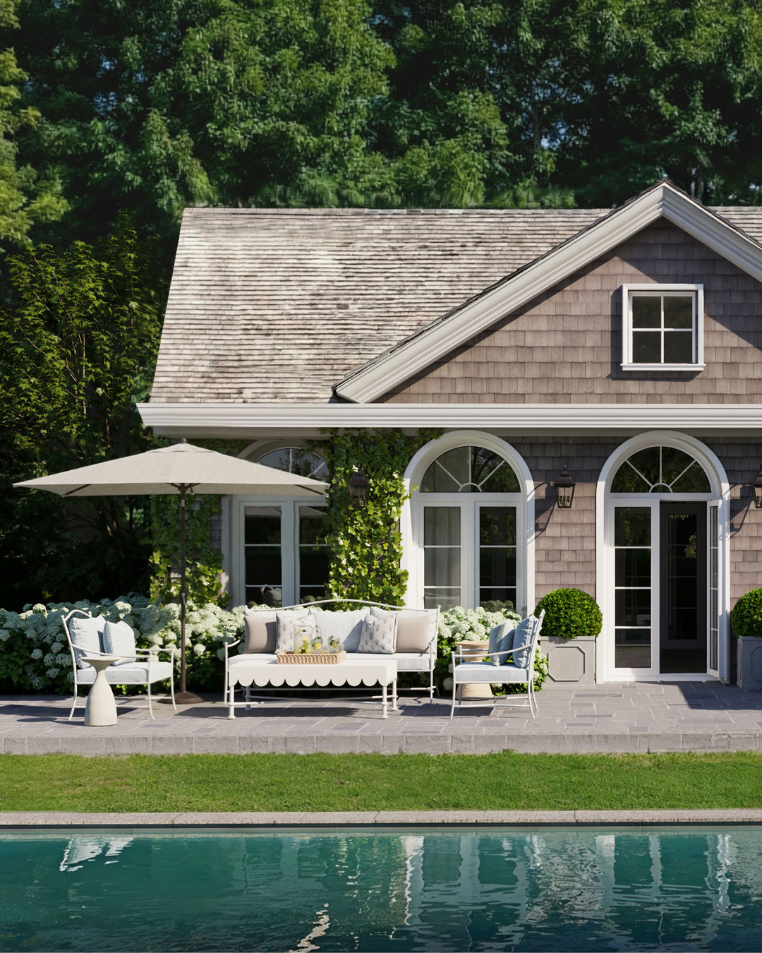 a pool house with weathered shingle siding and a lounge area in front with a Sunbrella sofa, Sunbrella armchairs, and a scalloped outdoor coffee table